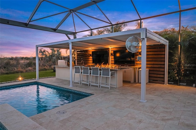 pool at dusk featuring a bar, a lanai, a patio, and exterior kitchen