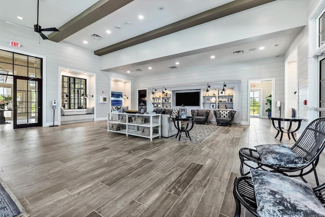 living room with beamed ceiling, a towering ceiling, wooden walls, and hardwood / wood-style floors