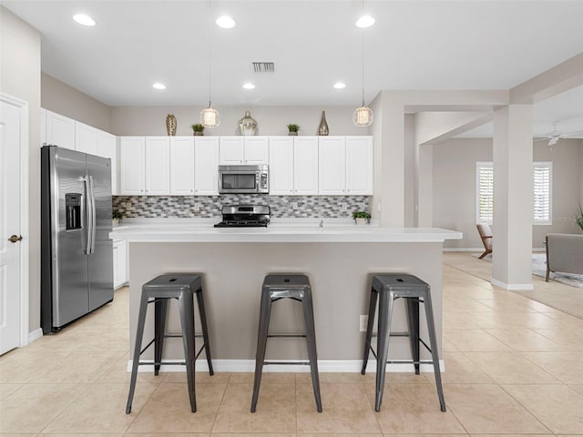 kitchen featuring stainless steel appliances, a kitchen breakfast bar, decorative light fixtures, and a kitchen island with sink