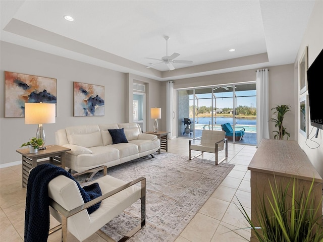 living room featuring ceiling fan, a tray ceiling, and light tile patterned floors