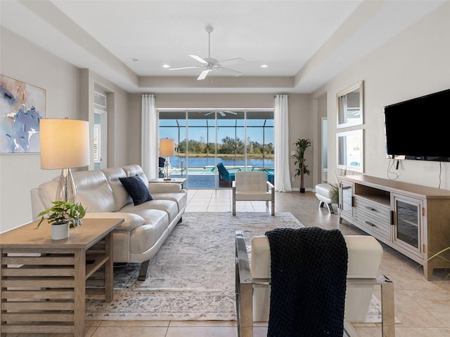 living room featuring a raised ceiling, ceiling fan, and light tile patterned flooring