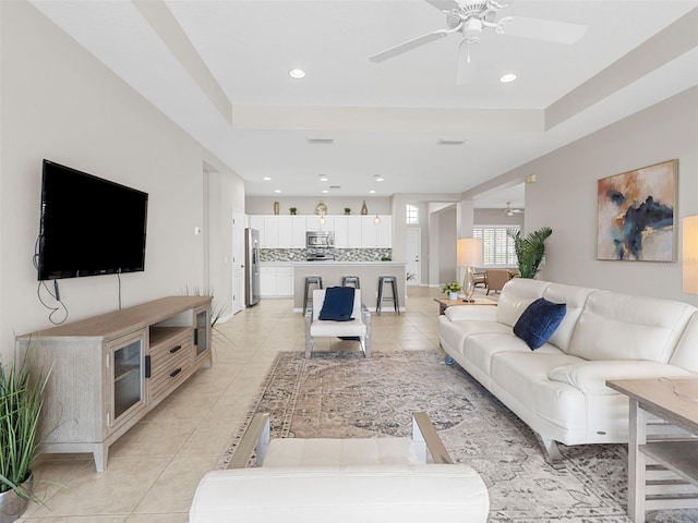 living room featuring a raised ceiling, light tile patterned floors, and ceiling fan