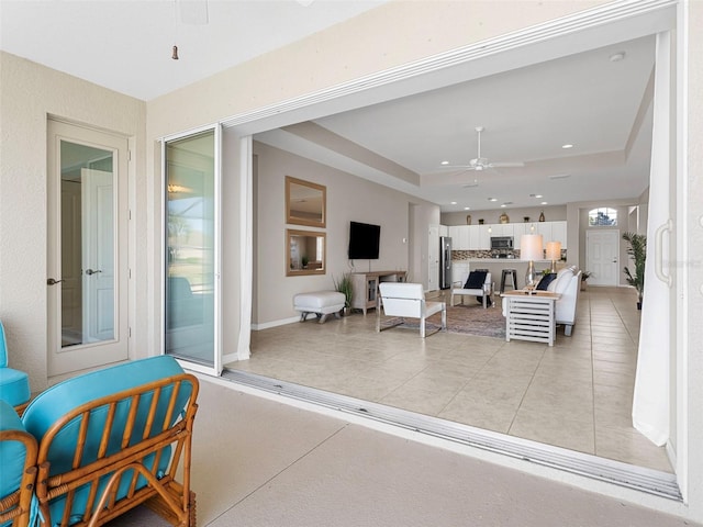 living room with light tile patterned floors, a tray ceiling, and ceiling fan