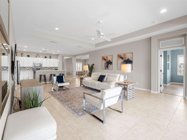 tiled living room featuring a raised ceiling and ceiling fan