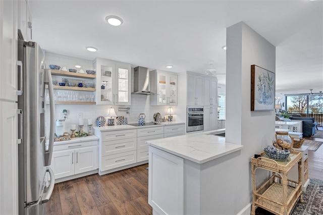 kitchen featuring dark hardwood / wood-style floors, white cabinets, stainless steel appliances, light stone countertops, and wall chimney range hood