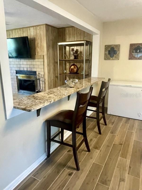 bar with fridge, light stone countertops, and a brick fireplace