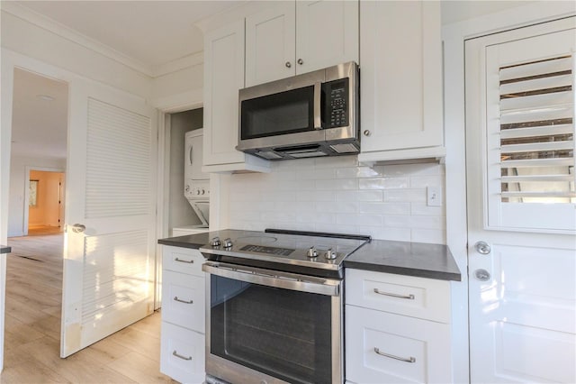 kitchen with crown molding, appliances with stainless steel finishes, stacked washer / dryer, decorative backsplash, and white cabinets