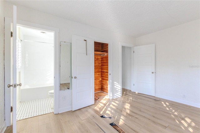 unfurnished bedroom featuring ensuite bath, light hardwood / wood-style flooring, a closet, and a textured ceiling