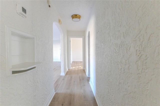 hall with a textured ceiling and light wood-type flooring