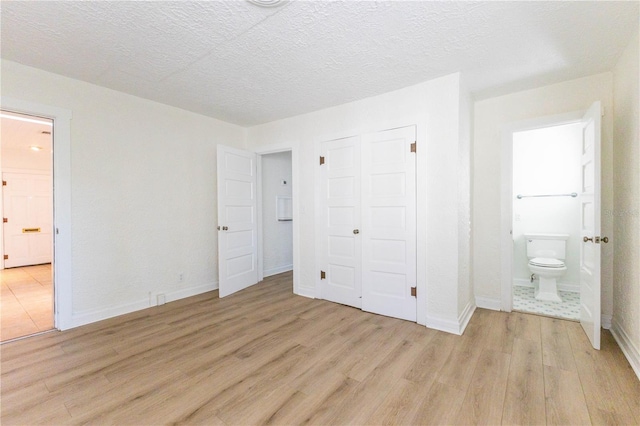 unfurnished bedroom with a closet, a textured ceiling, ensuite bath, and light hardwood / wood-style flooring