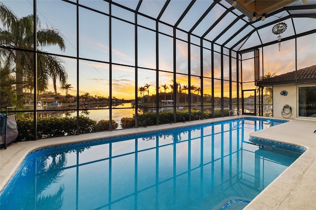 pool at dusk featuring a water view and a lanai