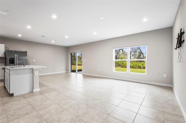 kitchen featuring a kitchen island with sink, light tile patterned floors, stainless steel fridge, and white cabinets