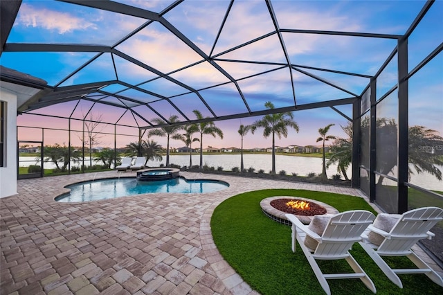 pool at dusk with a lanai, an outdoor fire pit, a water view, a patio area, and an in ground hot tub