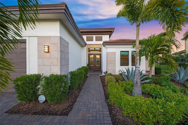 exterior entry at dusk featuring a garage and french doors