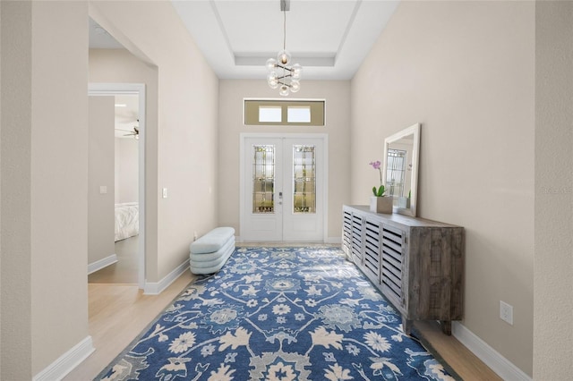 foyer entrance with a tray ceiling, light hardwood / wood-style floors, french doors, and a chandelier