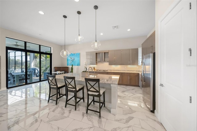 kitchen featuring pendant lighting, stainless steel fridge, a breakfast bar, light stone countertops, and a center island with sink