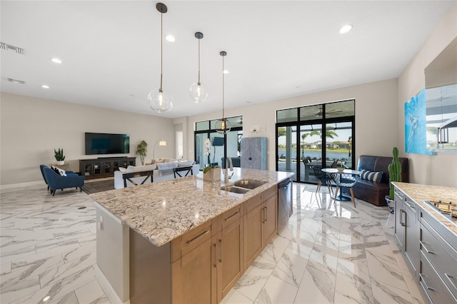 kitchen with sink, a kitchen island with sink, light stone countertops, decorative light fixtures, and stainless steel dishwasher