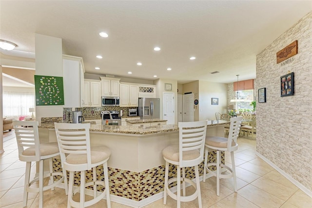 kitchen with light tile patterned flooring, appliances with stainless steel finishes, a kitchen breakfast bar, light stone counters, and kitchen peninsula