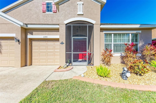 doorway to property featuring stucco siding, an attached garage, and driveway