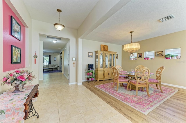 dining room with light wood-type flooring, baseboards, visible vents, and a textured ceiling