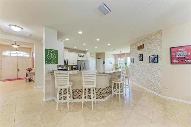 kitchen featuring a breakfast bar, light stone countertops, visible vents, and stainless steel appliances