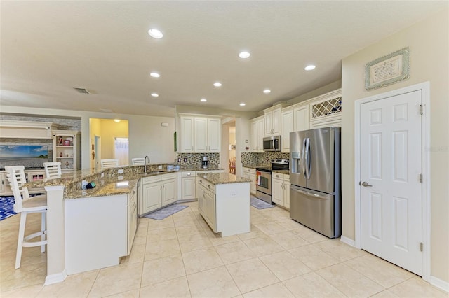 kitchen featuring a breakfast bar, a peninsula, stainless steel appliances, and light stone countertops