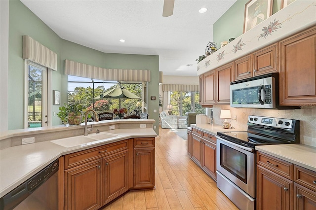 kitchen with appliances with stainless steel finishes, tasteful backsplash, sink, a textured ceiling, and light hardwood / wood-style flooring