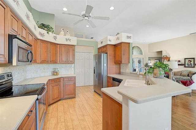 kitchen featuring sink, tasteful backsplash, light wood-type flooring, appliances with stainless steel finishes, and kitchen peninsula