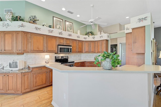 kitchen with a towering ceiling, decorative backsplash, kitchen peninsula, stainless steel appliances, and light wood-type flooring