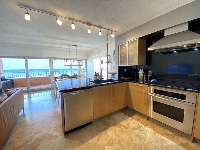 kitchen with hanging light fixtures, kitchen peninsula, stainless steel appliances, a water view, and wall chimney exhaust hood