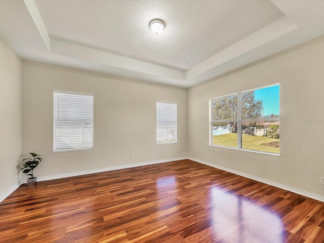 empty room with wood-type flooring, a textured ceiling, and a tray ceiling
