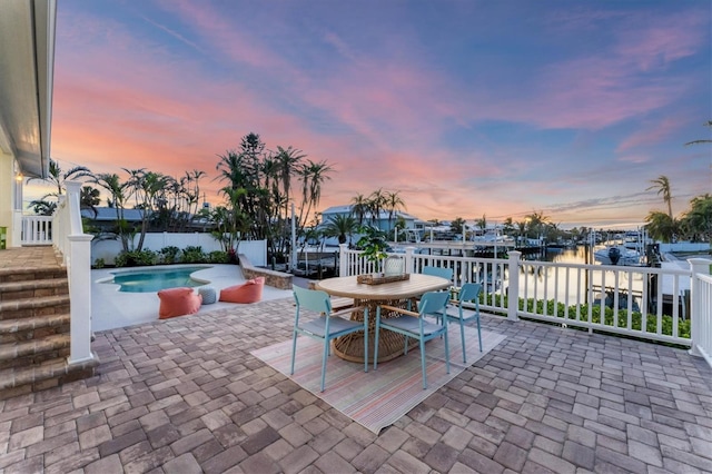 patio terrace at dusk with a fenced in pool and a water view