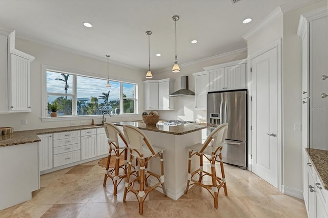 kitchen featuring wall chimney range hood, appliances with stainless steel finishes, white cabinets, a kitchen island, and dark stone counters