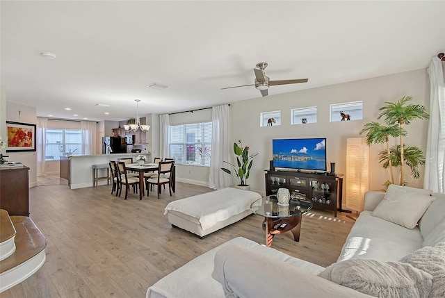 living room featuring ceiling fan with notable chandelier and light hardwood / wood-style flooring