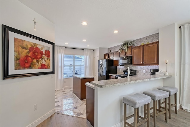 kitchen featuring decorative backsplash, black appliances, kitchen peninsula, and a breakfast bar