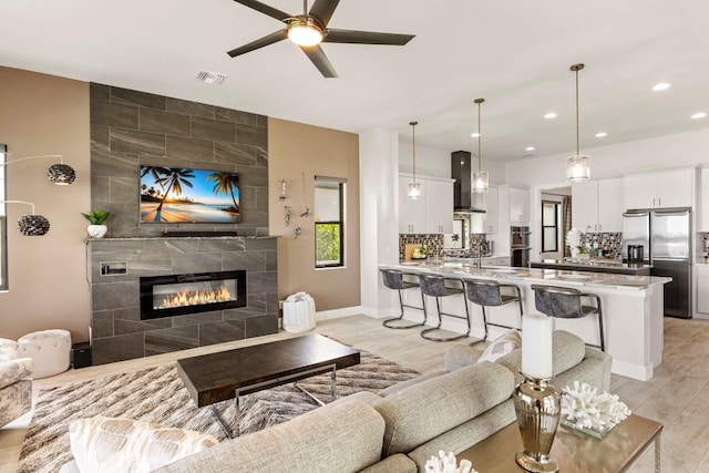 living room featuring a fireplace, ceiling fan, and light wood-type flooring