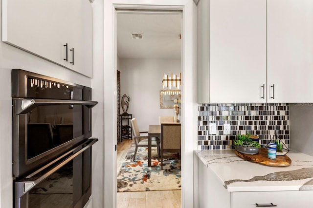 kitchen featuring multiple ovens, white cabinets, and light stone counters