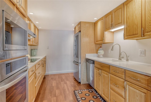 kitchen with stainless steel appliances, sink, light brown cabinets, and light hardwood / wood-style flooring