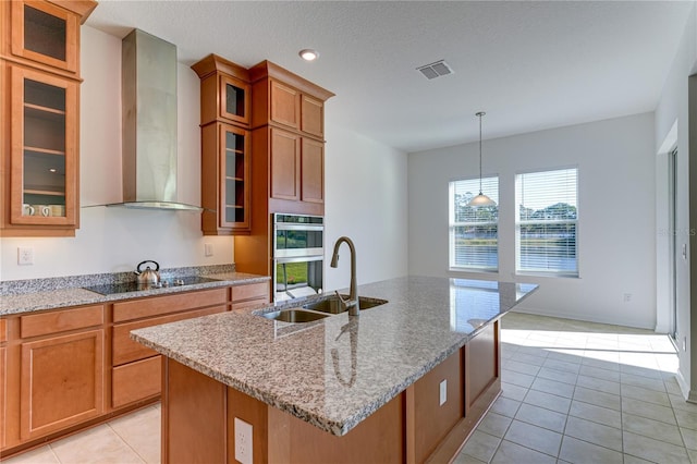 kitchen with sink, a center island with sink, black electric cooktop, pendant lighting, and wall chimney range hood