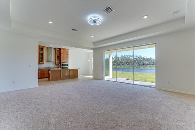 unfurnished living room with light carpet, a tray ceiling, and a water view