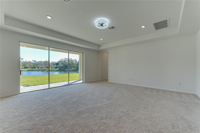 carpeted spare room with a raised ceiling and a water view