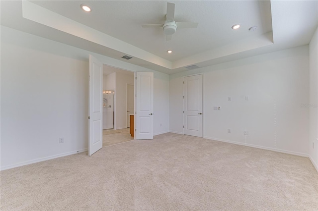 unfurnished bedroom featuring ceiling fan, a tray ceiling, and light carpet