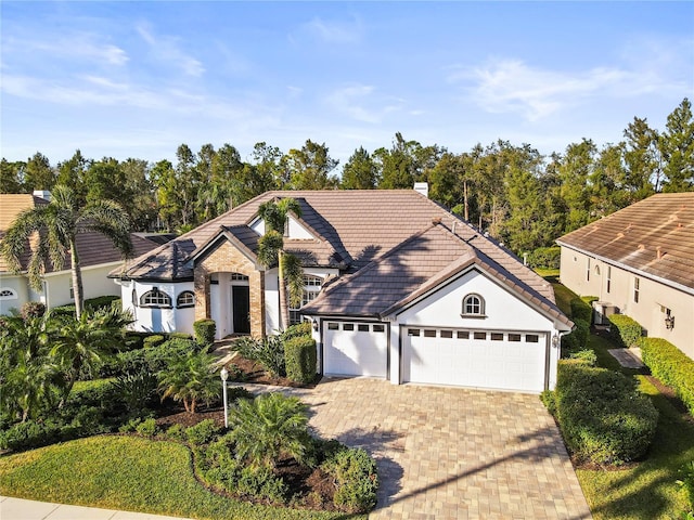 view of front of home with a chimney, decorative driveway, a tiled roof, and an attached garage