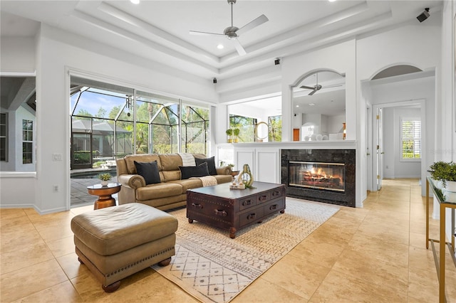 living room featuring a fireplace, a raised ceiling, a ceiling fan, a sunroom, and baseboards