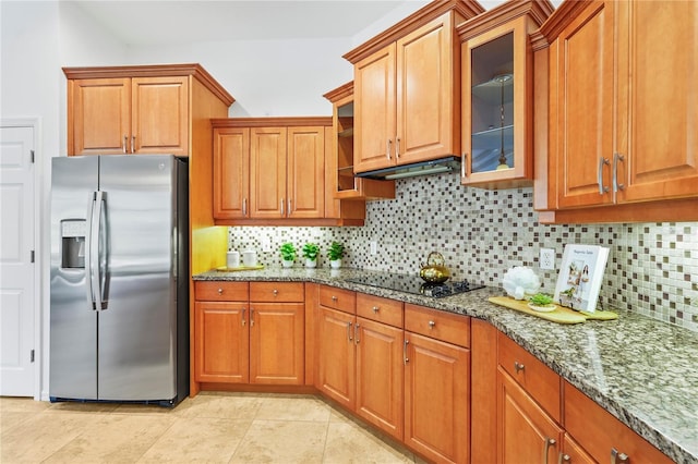 kitchen featuring stone countertops, brown cabinetry, stainless steel fridge with ice dispenser, glass insert cabinets, and black electric cooktop