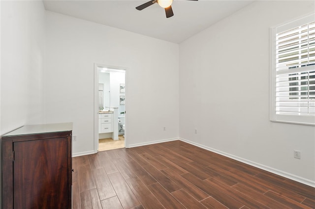 unfurnished bedroom with dark wood-style floors, connected bathroom, ceiling fan, and baseboards