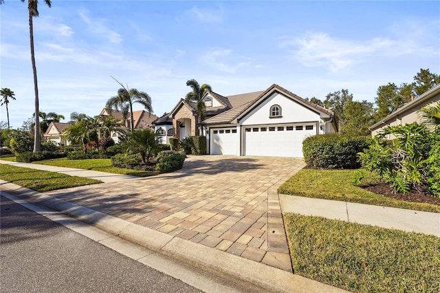 view of front facade with a front yard, decorative driveway, a tile roof, and an attached garage