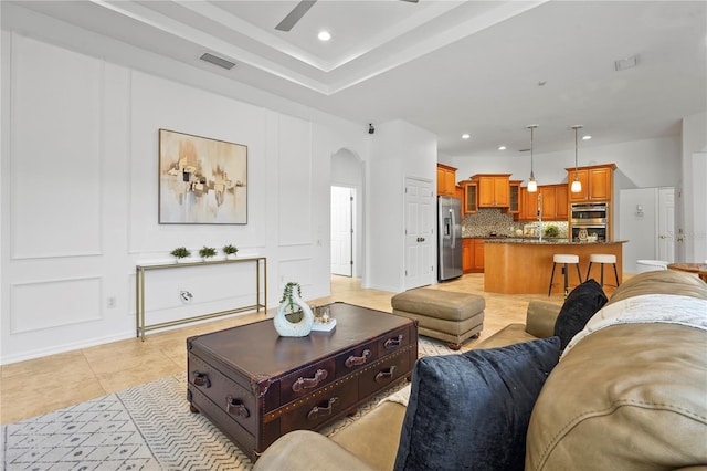 living area with light tile patterned floors, visible vents, arched walkways, a decorative wall, and recessed lighting