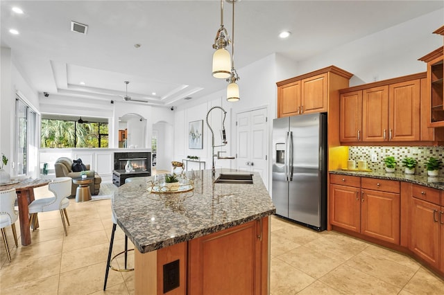 kitchen featuring a tray ceiling, pendant lighting, a center island with sink, visible vents, and stainless steel fridge