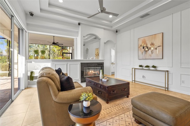 living area with a tray ceiling, a fireplace, light tile patterned floors, visible vents, and a decorative wall